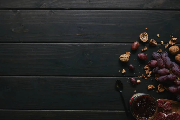 Top view of fresh ripe grapes, walnuts, sliced salami and jam on wooden background — Stock Photo