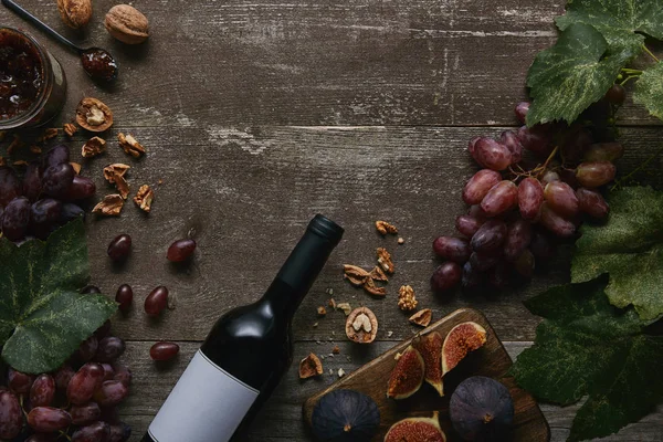 Draufsicht auf Weinflasche mit leerem Etikett, Früchten und köstlicher Marmelade auf Holztisch — Stockfoto