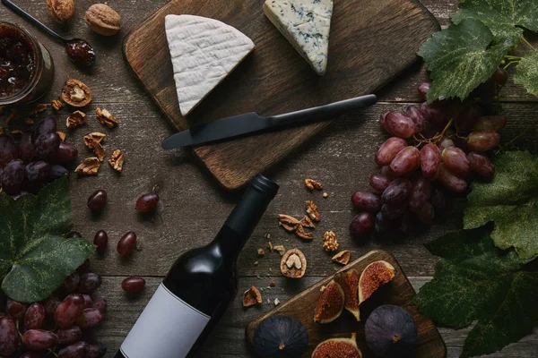 Top view of wine bottle with blank label and delicious cheese on wooden table — Stock Photo