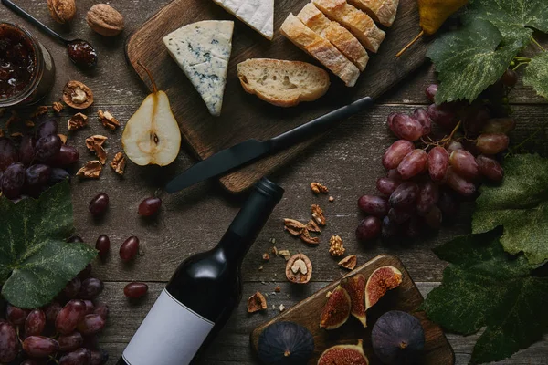 Vista superior de garrafa de vinho com rótulo em branco, frutas frescas e deliciosos lanches na mesa de madeira — Fotografia de Stock