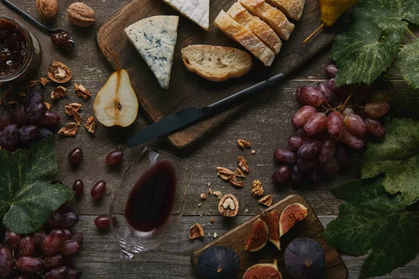 Top view of red wine in glass, fresh fruits and delicious snacks on wooden table — Stock Photo