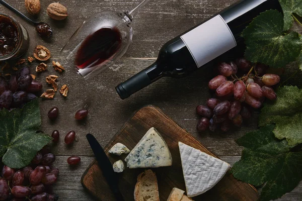 Vista superior de botella y copa de vino tinto, delicioso queso y uvas en mesa de madera — Stock Photo