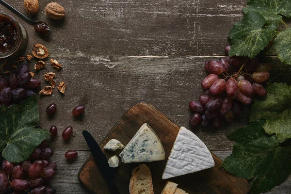 Vue de dessus de raisins frais mûrs avec feuilles vertes, noix, délicieux fromage et confiture sur table en bois — Photo de stock