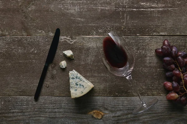 Top view of glass with red wine, cheese, grapes and knife on wooden table — Stock Photo