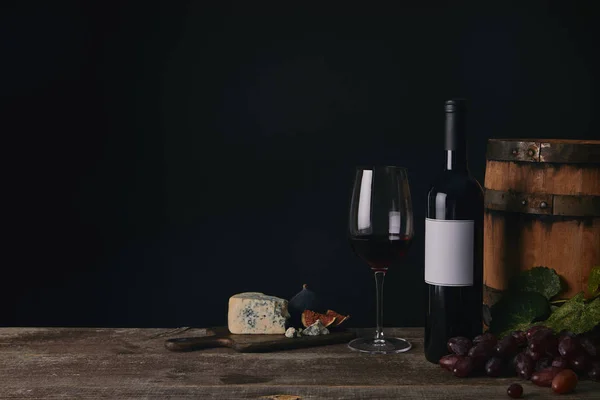 Vue rapprochée du verre, de la bouteille et du tonneau de vin avec fromage et raisins sur fond noir — Photo de stock