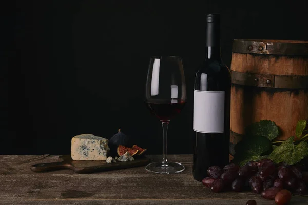 Vista ravvicinata di vetro, bottiglia e botte di vino con formaggio e uva sul tavolo di legno — Foto stock
