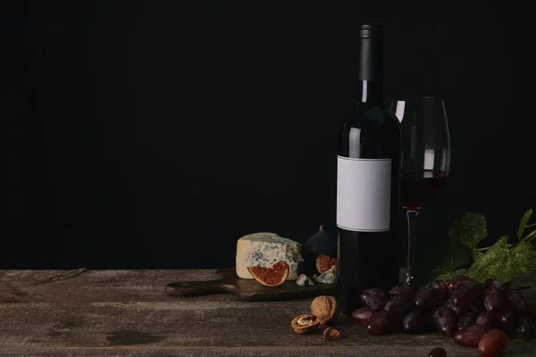 Bottle and glass of red wine, grapes and cheese on wooden table — Stock Photo