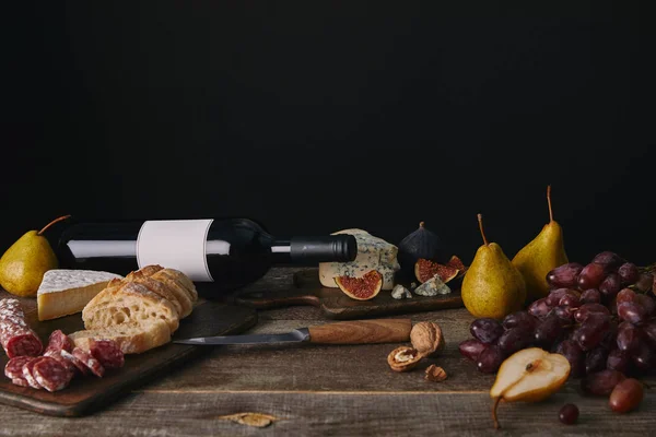 Garrafa de vinho com rótulo em branco, frutas, lanches deliciosos e faca na mesa de madeira — Fotografia de Stock