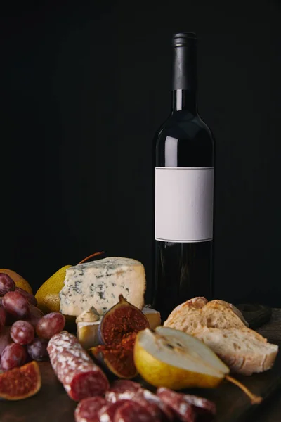 Пляшка вина з порожньою етикеткою і смачними закусками на чорному — стокове фото