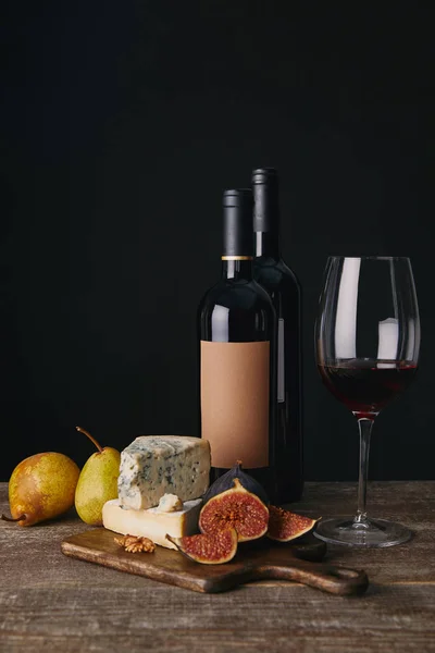 Vista de cerca de las botellas y la copa de vino tinto, delicioso queso, higos y peras en la mesa de madera - foto de stock