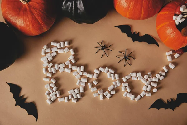 Hochwinkelaufnahme von Halloween-Kürbissen mit Papierfledermäusen und Wortbuh aus Marshmallows auf beigem Tisch — Stockfoto