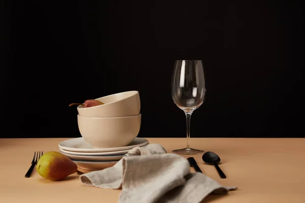 Plates, bowls, wineglass, napkin and pears on beige table — Stock Photo