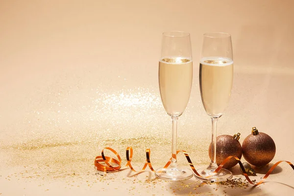 Christmas balls, wavy ribbon and two glasses of champagne with sequins on tabletop — Stock Photo