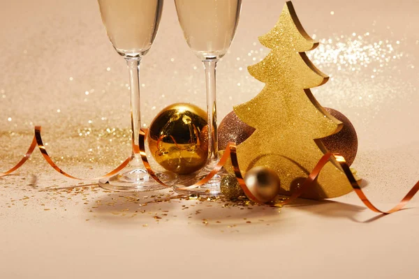 Рождественские игрушки, золотая елка и два бокала шампанского с блестками на столе — стоковое фото