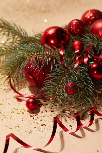 Juguetes de Navidad brillantes rojos, cinta ondulada y rama de pino en la superficie brillante - foto de stock