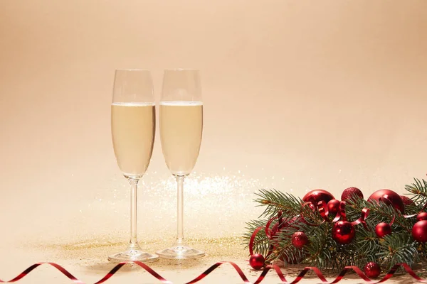 Glasses of champagne, red shiny christmas balls and pine branch on tabletop with sequins — Stock Photo