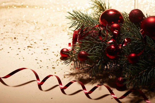 Giocattoli di Natale lucidi rossi, nastro ondulato e ramo di pino sulla superficie lucida — Foto stock