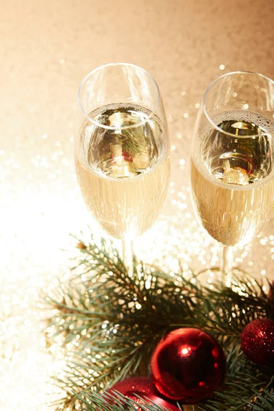 Vista de ángulo alto de copas de champán, bolas de Navidad y rama de pino en la mesa brillante - foto de stock