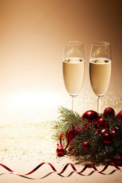 Dois copos de champanhe, bolas de Natal vermelho brilhante e ramo de pinho em mesa brilhante — Fotografia de Stock