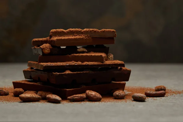 Vista de cerca de piezas de chocolate gourmet dulce con nueces y granos de cacao en gris - foto de stock