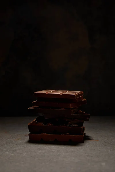 Vue rapprochée de délicieux morceaux de chocolat empilés sur fond noir — Photo de stock