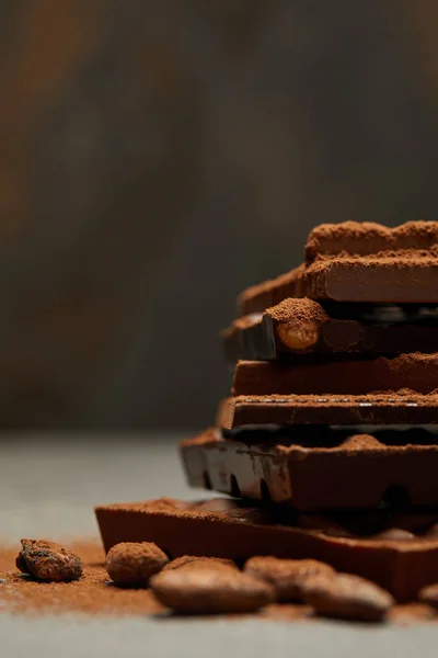 Vista ravvicinata di deliziosi pezzi assortiti di cioccolato impilati con noci e fagioli di cacao su grigio — Foto stock