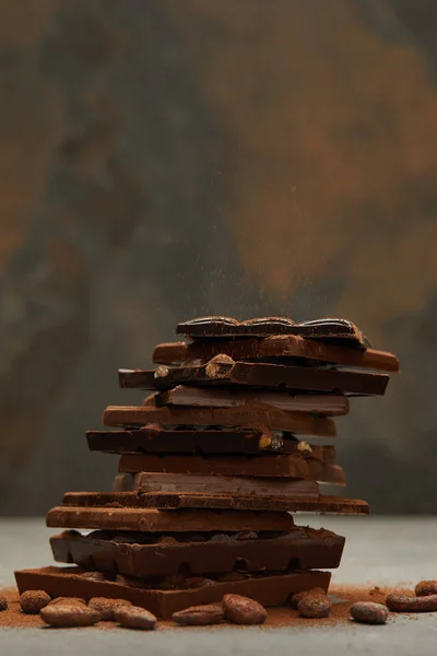 Vista ravvicinata di deliziosi pezzi di cioccolato assortiti impilati e noci sul grigio — Foto stock