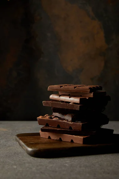 Morceaux de chocolat gastronomique assortis sur planche à découper en bois sur gris — Photo de stock