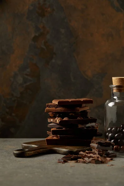 Deliciosas piezas de chocolate surtidos en la tabla de cortar y bolas de chocolate gourmet en frasco de vidrio - foto de stock