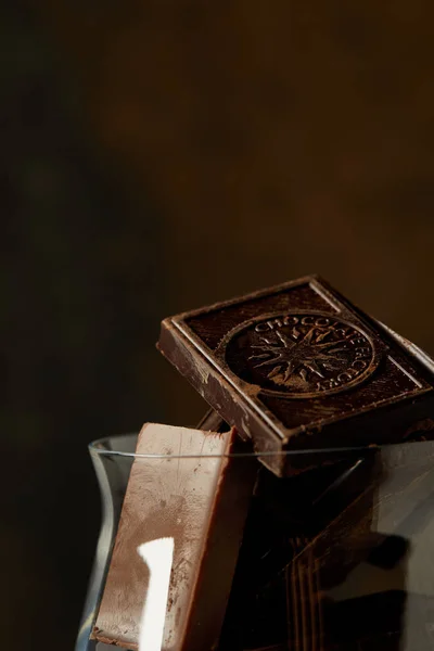 Vista de perto de pedaços de chocolate gourmet em vidro no fundo escuro — Fotografia de Stock