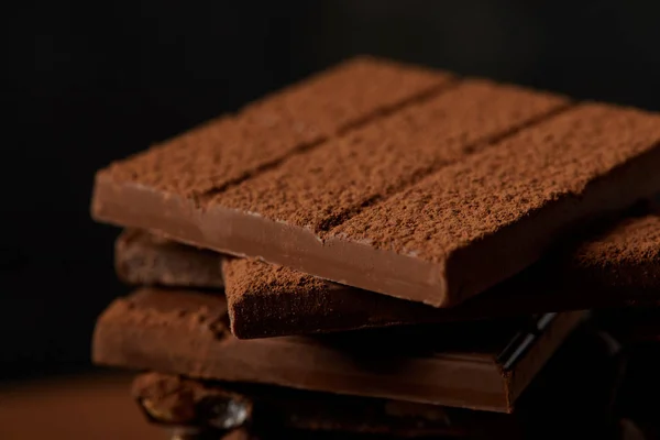 Vista close-up de deliciosas barras de chocolate sortidas com cacau em pó em preto — Fotografia de Stock