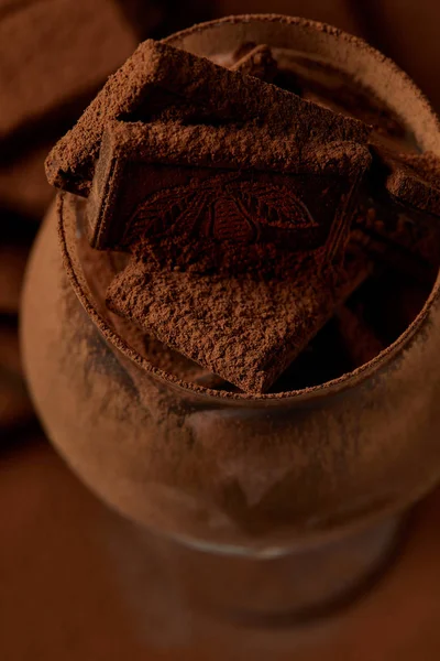 Vue rapprochée du verre avec morceaux de chocolat gastronomique et poudre de cacao — Photo de stock