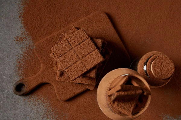 Вид сверху на вкусные кусочки шоколада с какао-порошком на доске — стоковое фото