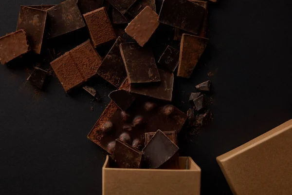 Vue du dessus de la boîte et délicieux morceaux de chocolat assortis sur noir — Photo de stock