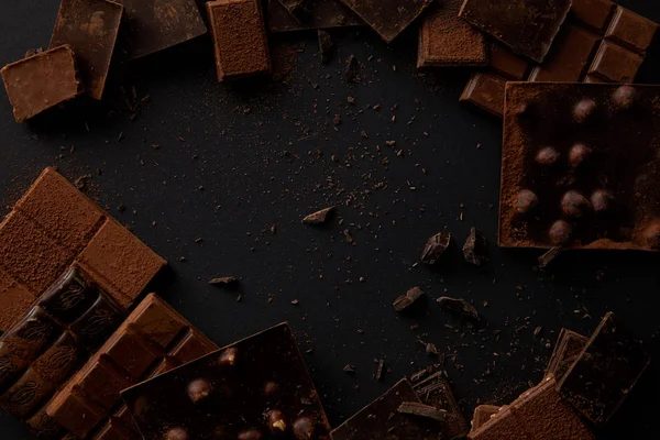 Vista superior de várias deliciosas peças de chocolate no fundo preto — Fotografia de Stock