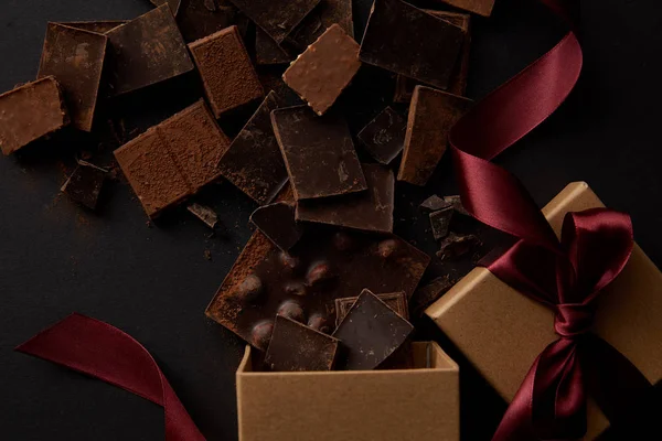 Vue du dessus des boîtes-cadeaux et de délicieux morceaux de chocolat sur noir — Photo de stock