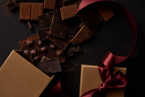 Vista dall'alto di pezzi di cioccolato gourmet con noci e confezione regalo su nero — Foto stock