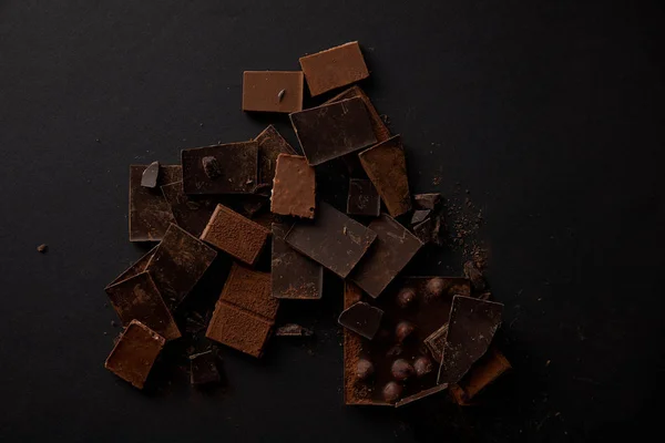 Vue de dessus des morceaux de chocolat gastronomique aux noisettes sur noir — Photo de stock