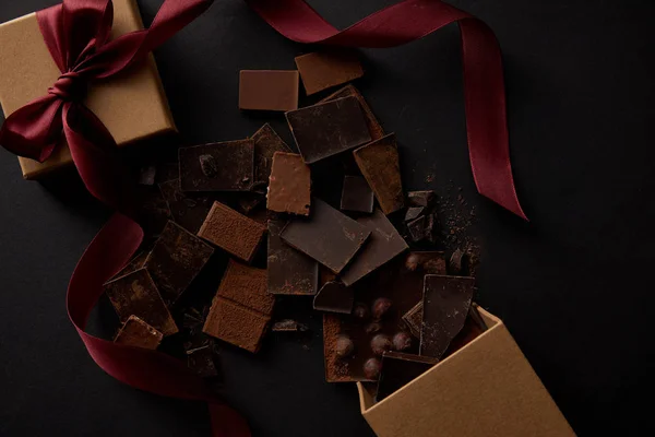 Вид зверху смачні шоколадні шматочки з горіхами та подарунковою коробкою на чорному — стокове фото