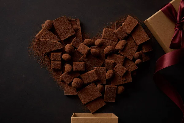 Vue du dessus du chocolat savoureux avec des noix et de la poudre de cacao disposés en forme de coeur et boîte cadeau sur noir — Photo de stock