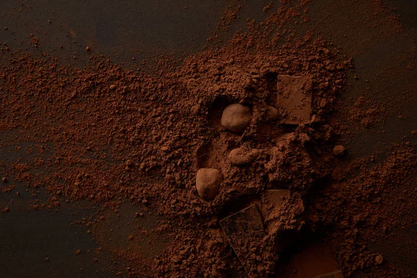Vista superior de deliciosas piezas de chocolate y cacao en polvo gourmet sobre fondo oscuro - foto de stock
