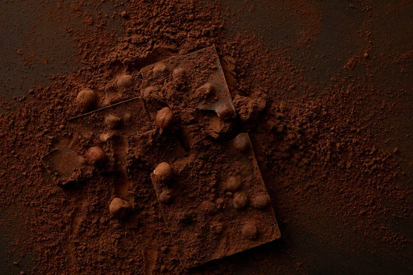 Вид сверху на вкусные кусочки шоколада с орехами на темном фоне — стоковое фото