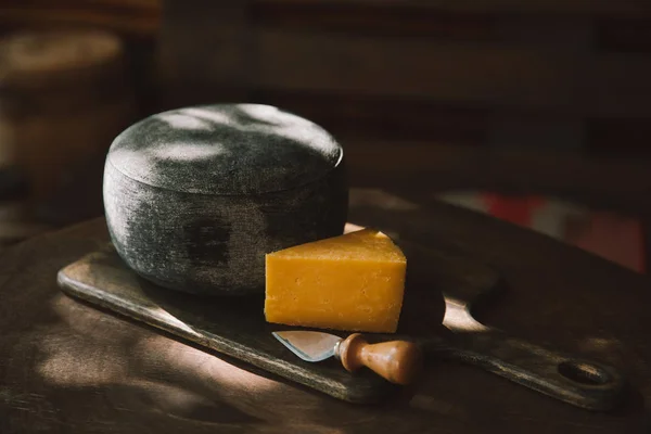 Primer plano de queso y cuchillo en tabla de cortar de madera - foto de stock