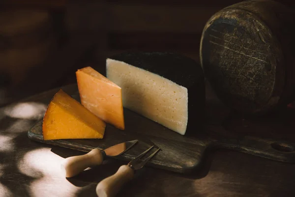 Различные виды вкусного сыра с сырными столовыми приборами на деревенском деревянном столе — стоковое фото