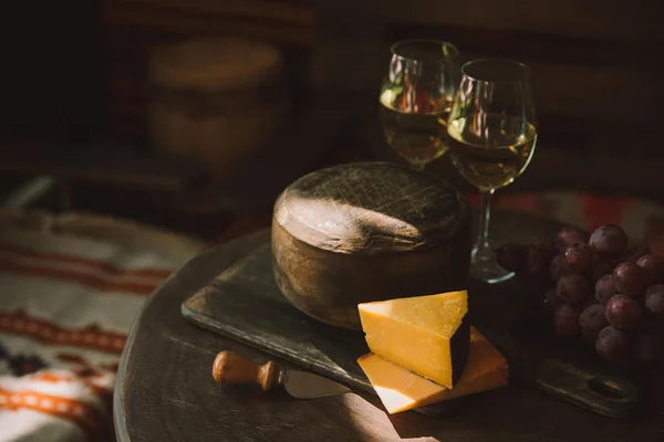 Queso en rodajas con vino y uvas sobre tabla de cortar de madera - foto de stock