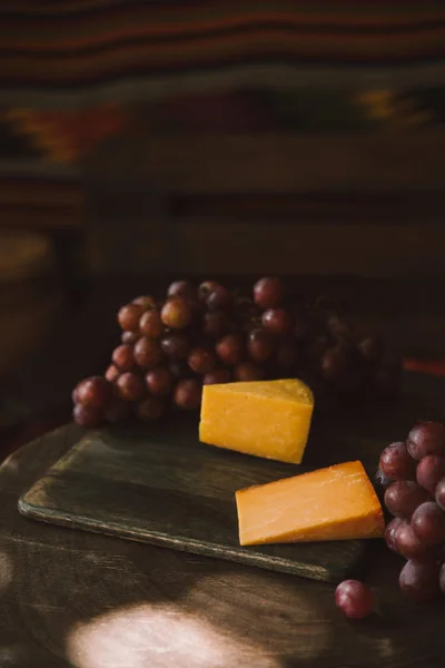 Close-up shot of slices of cheese with grapes on cutting board — Stock Photo