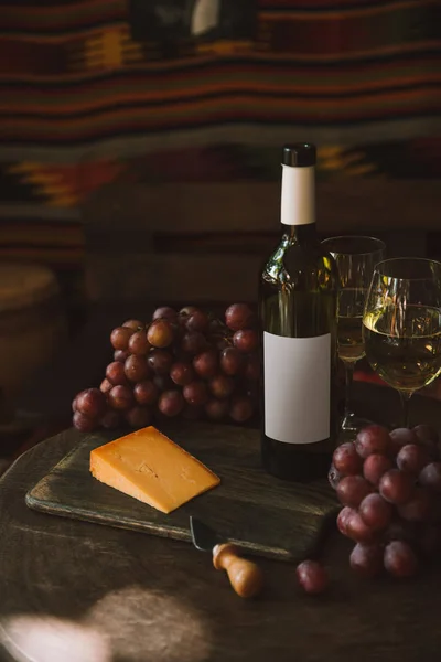 Nahaufnahme einer Käsescheibe mit Messer, Trauben und Weißwein auf Schneidebrett — Stockfoto
