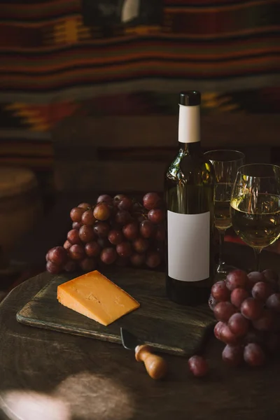 Close-up shot of slice of cheese with knife, grapes and white wine on cutting board — Stock Photo