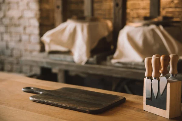 Tagliere vuoto con coltelli da formaggio sul supporto sul tavolo di legno nella fabbricazione del formaggio — Foto stock