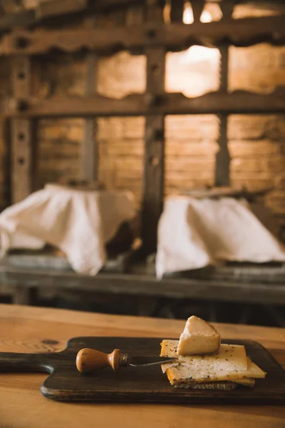 Sliced cheese with knife on wooden cutting board — Stock Photo